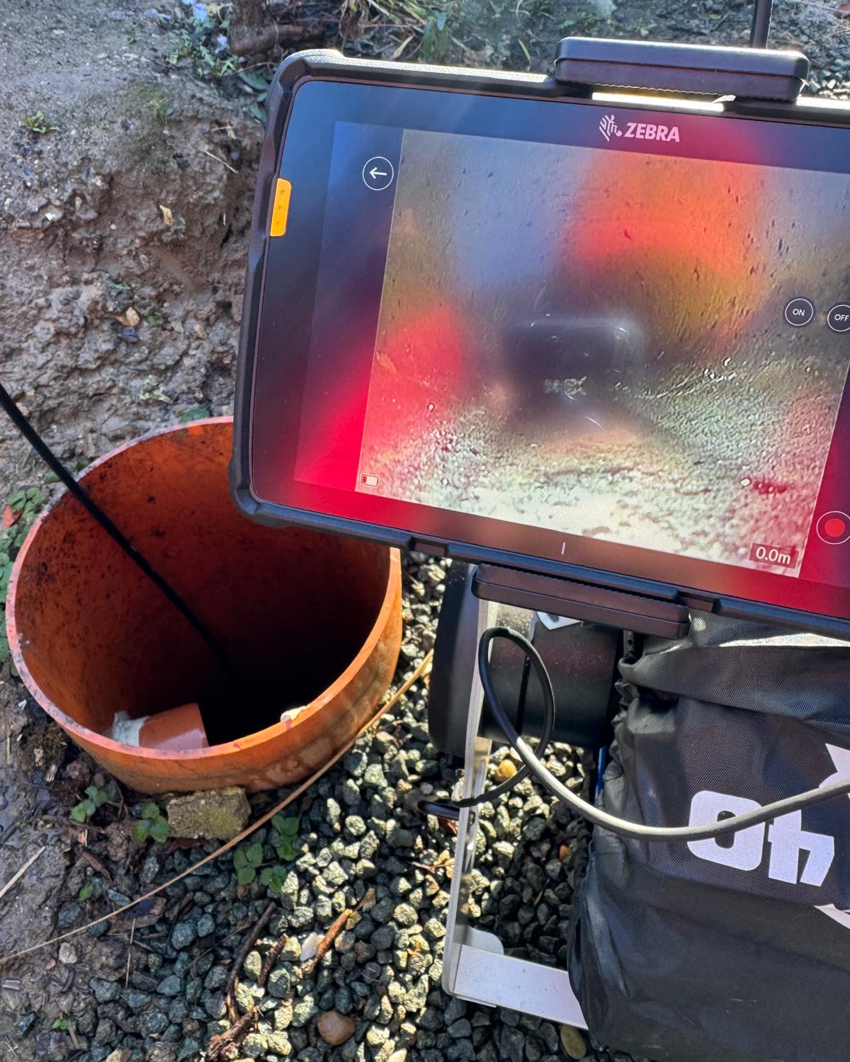 Inspection camera tablet above an open access pit, the inside of the pipe on screen.