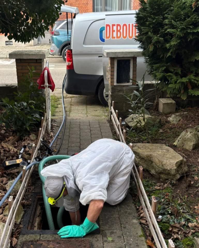 Technician leaning into an inspection chamber outside a house, the van parked on the street.